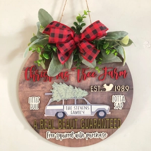 Close-up of wooden Christmas sign with red plaid bow, greenery, and farmhouse text