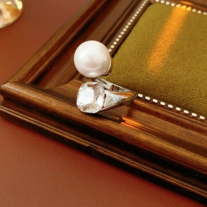 Macro detail of open ring featuring a white pearl and square crystal on a vintage background