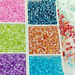 Close-up of colorful 6mm crackle glass beads sorted in a white storage box for DIY jewelry