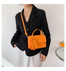 Detail of a bright orange quilted handbag with decorative gold chain and round charm