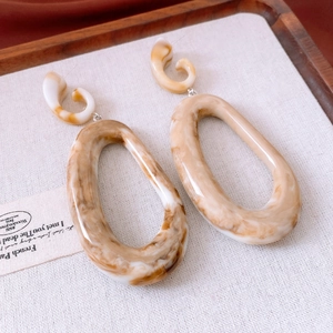 Detail of amber marble acrylic oval drop earrings on elegant linen texture background