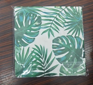 Close-up of stacked tropical napkins with green palm leaves and monstera prints in packaging