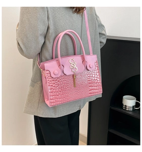 Close-up of pink crocodile texture crossbody bag with gold metal tassel and logo