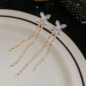 Macro shot of gold plated flower bow earrings with sparkling rhinestone tassels on ceramic
