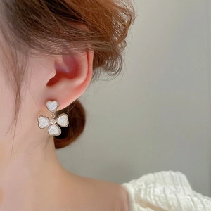 Gros plan d'une boucle d'oreille cœur et trèfle doré avec résine blanche sur l'oreille