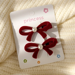 Detail of red velvet bow hair clips with white pearl on floral card and beige sweater