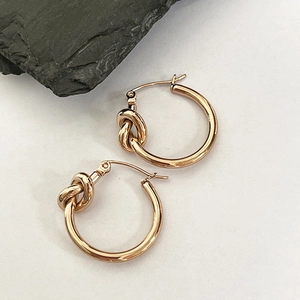 Macro shot of 18k gold plated stainless steel knot hoop earrings on a textured stone background