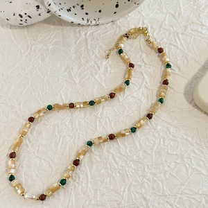 Detail of beaded necklace with shells, green and brown beads on a white fabric surface