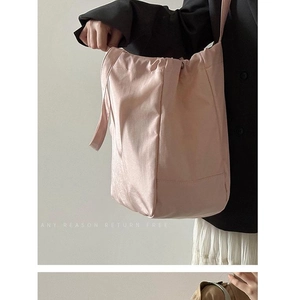 Detail of light pink satin tote bag with drawstring closure worn with a black suit