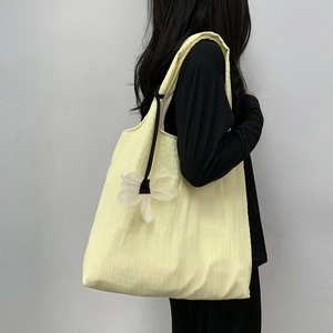 Detail of yellow pleated canvas tote bag with floral charm decoration on model shoulder