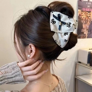 Close-up of fabric bow hair claw with black prints and a pearl pendant on a bun
