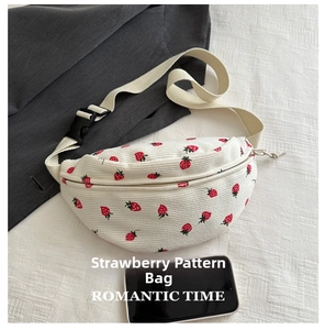 Close-up of white corduroy shoulder bag featuring red strawberry embroidery and buckle strap