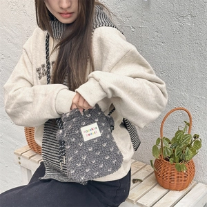 Gray plush crossbody bag with dots and rope strap worn by a model on a bench