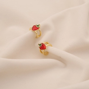 Macro shot of red strawberry ear cuffs with gold metal plating on beige fabric