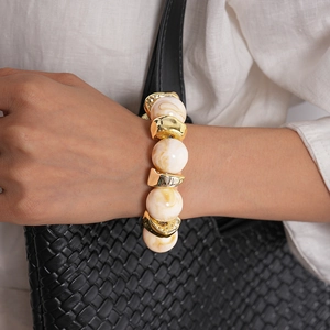 Dettaglio del bracciale con perle acriliche marmorizzate e metallo dorato sul polso