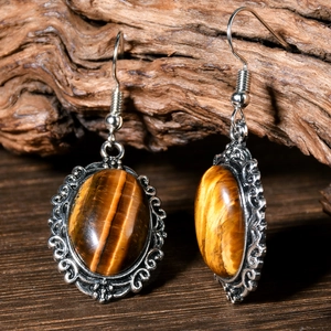 Macro shot of tiger eye stone earrings with vintage silver filigree on dark wood