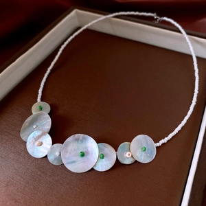 Detailed macro shot of white seed beads and iridescent shell pendants in a leather jewelry box