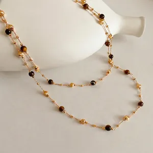 Double-layered gold-plated necklace with tiger eye beads draped on a white vase