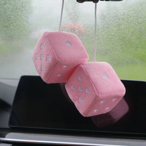 Close-up of pink plush car dice with white heart embroidery hanging on rearview mirror