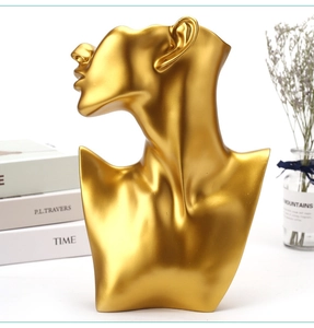 Golden resin bust necklace display stand with decorative dry flowers on a white desk