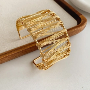 Gros plan d'un large bracelet manchette doré en fil métallique sur un plateau en bois
