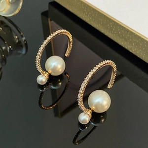 Detailed view of gold C-shaped earrings with pearls and rhinestones on black reflective surface
