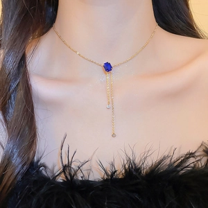 Detail of gold necklace with rectangular blue gemstone pendant and crystal tassels