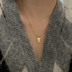 Close-up of a golden necklace featuring a bear pendant worn over a plaid sweater