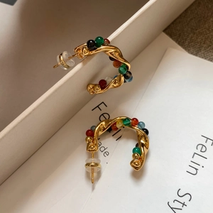 Macro view of twisted gold C-shaped earrings with colorful beads and bohemian details