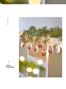 Detail of Santa Claus LED string lights with warm glow hanging on green pine branches