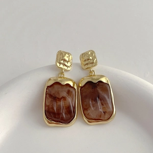Detail of vintage gold earrings with brown marbled resin squares on a stone pedestal