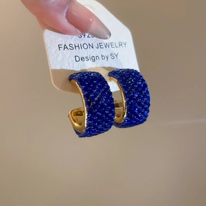 Macro shot of S925 silver needle and blue crystal encrusted gold C-shaped hoop earrings