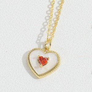 Detailed macro view of gold heart necklace with white pearl inlay and red zircon stone