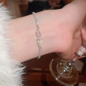 Detail of silver wavy zircon bracelet worn by a model holding a glass in social setting