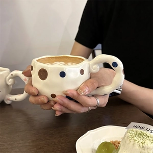 Handcrafted irregular ceramic coffee mug with blue and brown polka dots on a wooden table