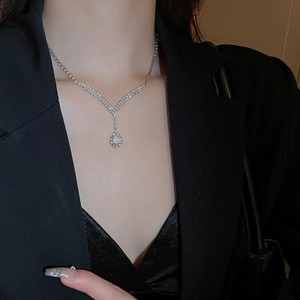 Close-up of silver V-shaped necklace with teardrop pendant worn by a model in black outfit