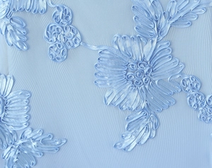 Vue macro des broderies florales en ruban bleu clair et du tissu en maille de la robe