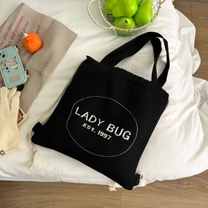 Detail des schwarzen Canvas-Tunnelzug-Rucksacks mit Lady Bug-Stickerei und Doppelgriffen
