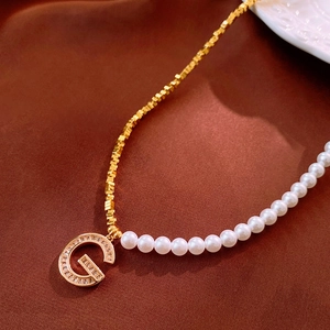 Détail macro du collier en or avec perle et pendentif lettre G en zircon