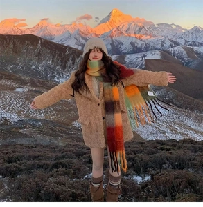 Rainbow plaid tassel scarf styled with camel wool coat against a snowy mountain backdrop