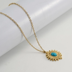 Detail of bohemian gold sunburst pendant with turquoise stone on white display
