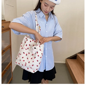 White corduroy bucket bag with strawberry pattern and plush charm on female model