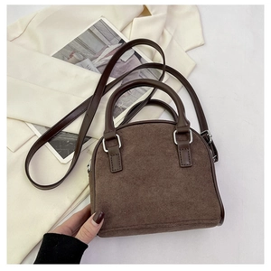 Close-up of brown suede shell bag featuring smooth leather handles and silver hardware