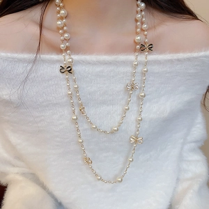 Detail view of a double-layered pearl necklace with enamel bows on a knit sweater