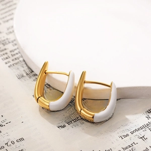 Close-up of gold U-shaped hoop earrings with white enamel on a vintage newspaper background