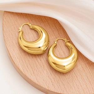 Macro shot of chunky gold water drop hoop earrings on a minimalist wooden display