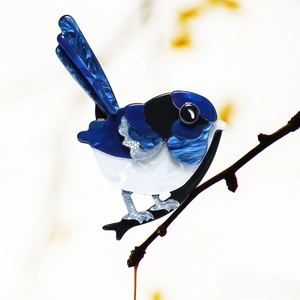 Detailed macro view of a blue and white acrylic bird brooch perched on a branch