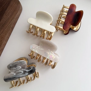 Top view of four acetate hair claw clips in beige, tortoiseshell, pearl and marble colors