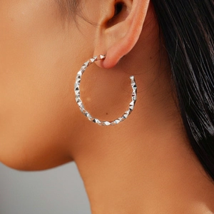 Macro detail of geometric faceted silver C-shape hoop earrings worn by a female model