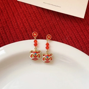 Macro shot of red and gold lion dance earrings with tassel beads on white ceramic tray